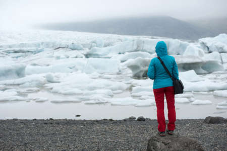 Tourist admiring the floating icebergs drifting in the water in Fjallsarlon glacier lagoon, Vatnajokull National Park, Iceland. Global warming, climate change conceptの写真素材