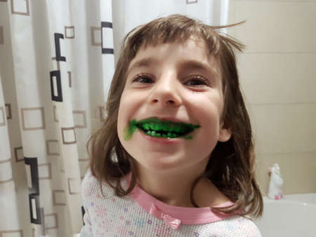 Young child showing green toothapaste on her teeth in the bathroom