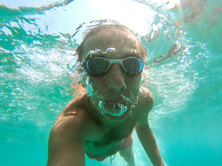 Underwater photo of a young active man swimming in turquoise sea waterの写真素材