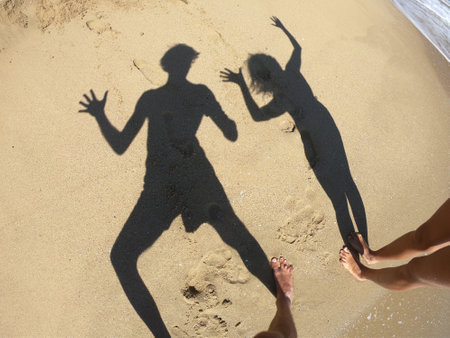 Shadow of a couple on a sandy beach and sea wavesの写真素材