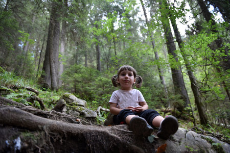 Cute toddler baby girl sitting on a tree trunk in the forestの写真素材