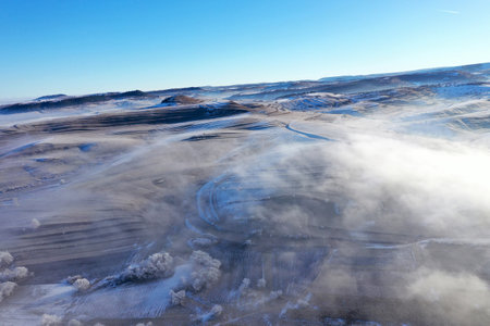 Aerial view of misty countryside hills at wintertime, morning fog above by droneの写真素材