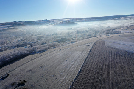 Aerial view of melting snow on hills on a misty sunny day by droneの写真素材