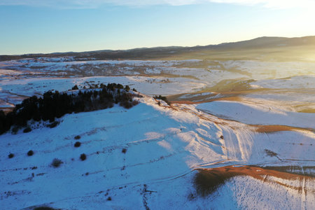 Flying over snowy winter hills in sunset lights by droneの写真素材