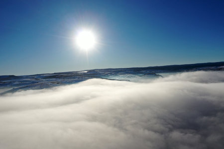 Aerial view of fog blankets a mountain landscape during a bright winter morning under a clear blue skyの写真素材