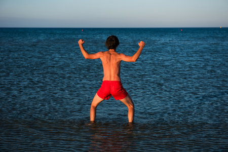 Slim guy posing in red swimwear in sea water.の写真素材