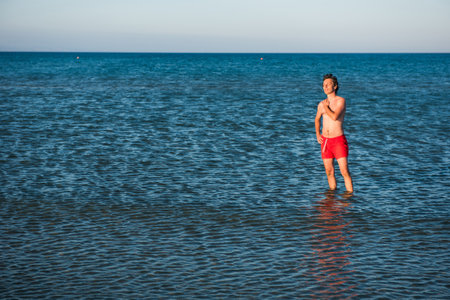 Slim guy posing in red swimwear in sea water.の写真素材