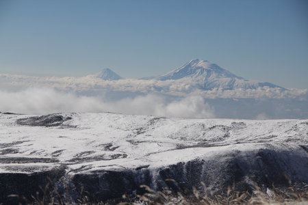 Breathtaking winter scenery with majestic snow-capped mountains glistening under the sun against a backdrop of a clear blue sky. Ideal for capturing the tranquil beauty of a winter wonderland.の写真素材