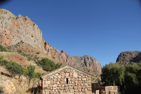 Small stone building in front of a rocky hillside under a clear blue sky. Rural architecture and natural landscape conceptの写真素材