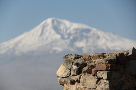Majestic Snowy Mountain Peak Towering Over Ancient Stone Wall Ruins in a Serene Landscapeの写真素材