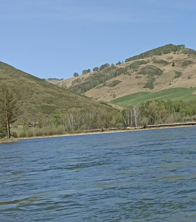 Experience the beauty of nature with a serene river flowing through lush green hills. The clear blue sky enhances the tranquility, making it perfect for nature and outdoor themes.の写真素材