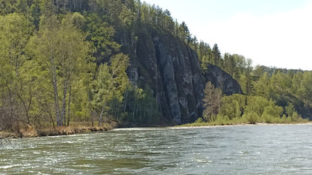 Discover a peaceful river flowing through a lush green forest, framed by a stunning rocky cliff. Ideal for tourism and inspiration, this scene captures the beauty of nature.の写真素材