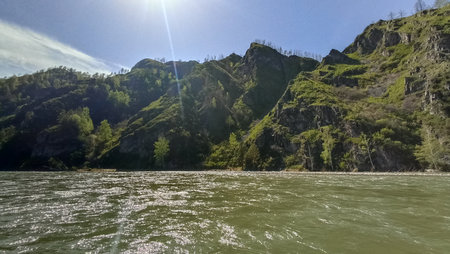 Breathtaking natural scenery showcasing a tranquil river beside impressive rocky mountain slopes covered with lush greenery, conveying the beauty of natural landscapes and serene outdoor environments.の写真素材