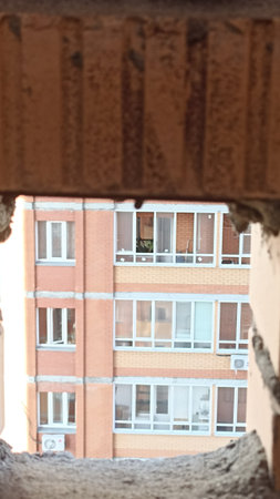 A rugged construction opening reveals a multi-story brick building with white-framed windows. The...