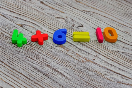 Math example from a colorful plastic numbers on a wooden background. School