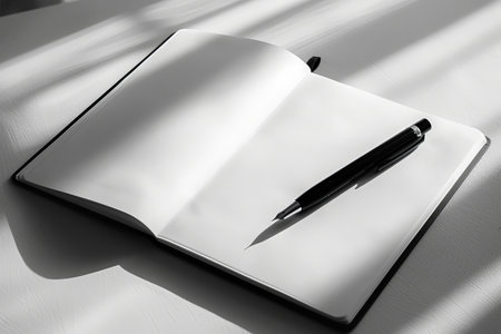 Notebook with pen on table in sunlight. Black and white.の素材