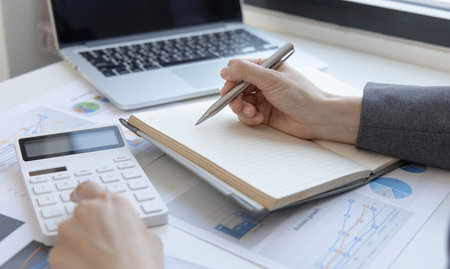 Head of accounting is recording the company's financial growth statistics using graphs as a reference for reviewing and analyzing the results, Taking notes and analyzing data graphs in office.の写真素材