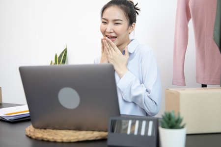 Young Asian woman congratulated and smiled as a large number of customers ordered her clothes online, Business of selling clothes on social media or selling online, Feel excited or surprise or shockedの写真素材