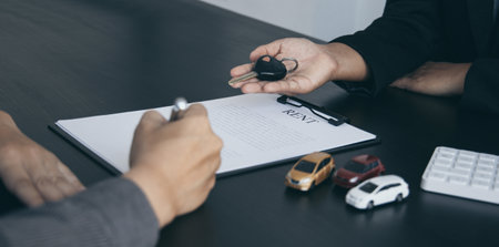 Female attendant handed over the rental car key to the customer who signed the contract and the terms of the agreement on the document, Car rental service concept.の写真素材