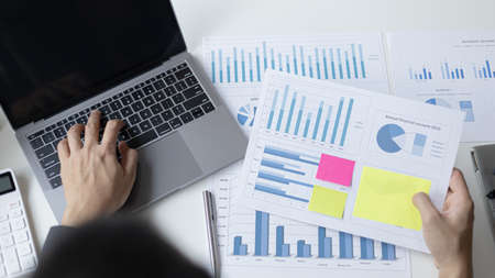 Young Asian office worker presses he finger on a laptop keyboard to analyze financial data and...