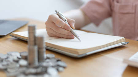 Dollar coins arranged in a slope graph, Blurred image of a businesswoman pressing a calculator, Take a notebook to record information, Saving money for business growth, Save money.の写真素材