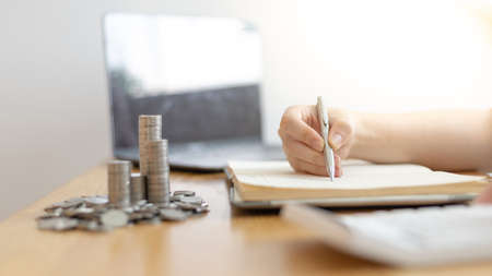Dollar coins arranged in a slope graph, Blurred image of a businesswoman pressing a calculator, Take a notebook to record information, Saving money for business growth, Save money.の写真素材