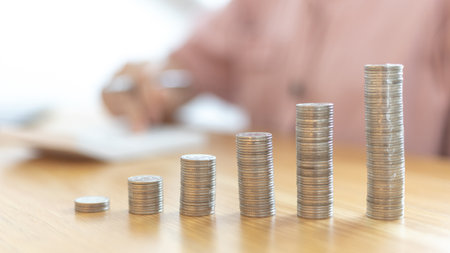 Dollar coins arranged in a slope graph, Blurred image of a businesswoman pressing a calculator, Financial business growth, Saving money for business growth or long-term profitability, Save money.の写真素材