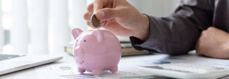 Businessmen put coins in a piggy bank and record income - income tax expenses in the office, Financial accounting and save money concept.の写真素材