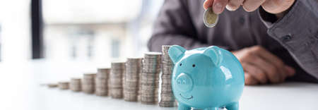 Businessmen put coins in a piggy bank and record income - income tax expenses in the office, Financial accounting and save money concept.の写真素材