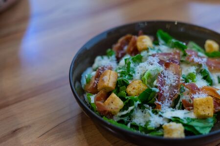 Caesar Salad with bacon in black plate on wooden backgroundの写真素材