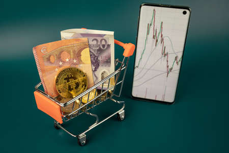 Gold Bitcoin and cash euro and pounds currency in mini trolley scene with mobile phone with line...