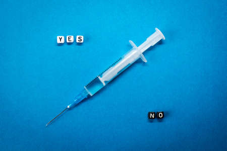 Yes No words made of square letters and a syringe on blue background. Pros and cons of coronavirus vaccine, concerns and doubts about COVID-19 vaccination conceptの写真素材