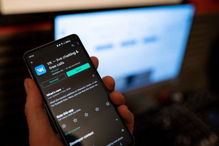 Hand with smartphone with VK app on Google Play, popular social network from Russia. Dark themeのeditorial素材