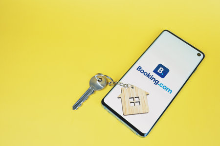 SWANSEA, UK - MARCH 31, 2021: Booking.com app logo displayed on smartphone, home key with house keyring on yellow background with copy spaceのeditorial素材