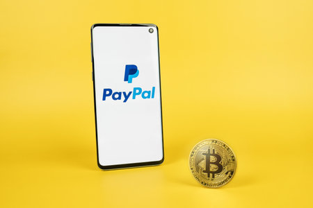 SWANSEA, UK - MARCH 31, 2021: PayPal logo on phone screen with Bitcoin cryptocurrency coin on yellow background. Checkout with crypto, new payment option conceptのeditorial素材