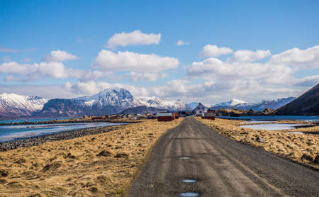 Rural road with potholes in Lofoten Islands, Norway. Village on a lake with mountains viewの写真素材
