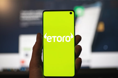 SWANSEA, UK - MAY 1, 2021: Man holding a smartphone with Etoro logo with blurred website as background. Trading platform, investing in stocks and cryptocurrenciesのeditorial素材
