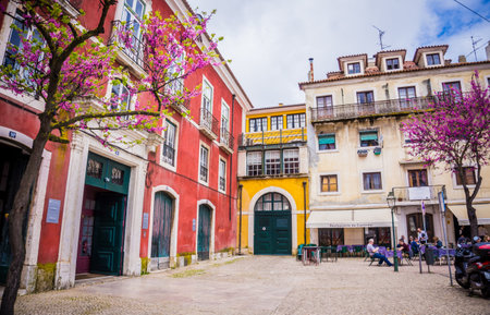 LISBON, PORTUGAL - MARCH 25, 2017: Typical colorful houses of Alfama in Lisbon, Portugal and blooming pink bougainvillea trees. Spring time. Yellow and red buildings with green doors.のeditorial素材