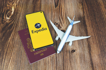 Expedia application logo on mobile phone screen with plane and passportのeditorial素材