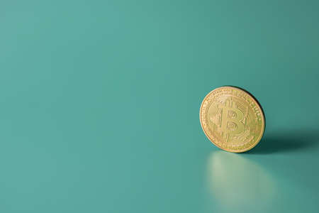 Bitcoin crypto gold single coin on green teal backround with copy space. Popular cryptocurrency bannerの写真素材