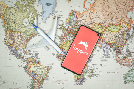 SWANSEA, UK - JUNE 19, 2021: Smartphone with Hopper app logo with plane toy on world map backround. Travel application, vacation planningのeditorial素材