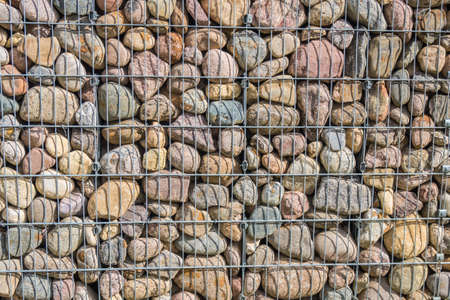 Gabion fence wall. Stone wall texture, rocks behind metal grid fence background.の写真素材