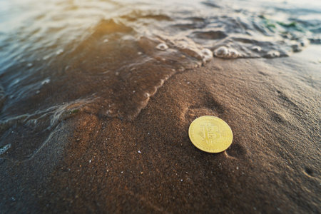 Bitcoin on the beach. Nature background with copy space. Single gold coin on the sand next to the water. Environment impact, using hydropower for mining conceptの写真素材