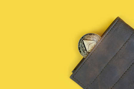 Ethereum or Eth crypto currency coin in a brown leather wallet on yellow background with copy space. Banner with space for text.の写真素材