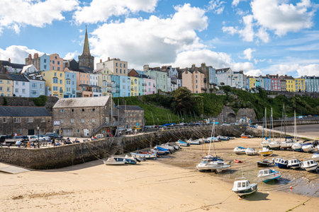 Tenby Harbour, Pembrokeshire, Wales, the United Kingdom. Boats on the beach at low tide. Colorful buildings of popular Welsh resort on a sunny Summer day. Tenby, UK - September 20, 2021のeditorial素材