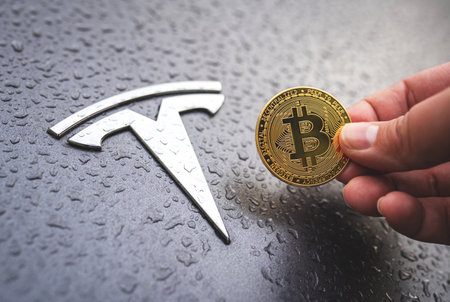 Bitcoin coin in hand with Tesla car logo on the background. Close-up, selective focus. Tesla accepts Bitcoin cryptocurrency concept. Warsaw, Poland - October 23, 2021のeditorial素材