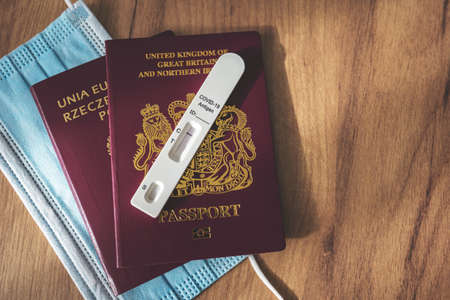 Negative rapid serology antigen COVID-19 test on red British and Polish passports and surgical face mask on wooden background. Travel during the coronavirus pandemic, avoid quarantine concept.の写真素材