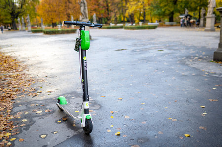 Lime rental electric scooter parked. A green and black ride sharing Lime e-scooter stands on sidewalk in Autumn park, no people. Warsaw, Poland - October 17, 2021.のeditorial素材
