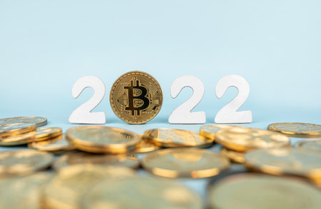 Bitcoin 2022 price prediction concept. Btc coin standing next to cryptocurrency tokens and year numbers on blue background. Close-up, soft focus.の写真素材
