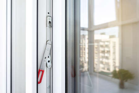 White plastic balcony door frame with fittings. Concealed drive lever close-up. Upvc windows and doors accessories and hardware.の写真素材
